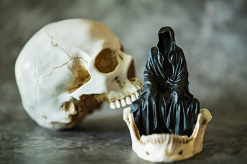 A statue of a grim reaper sitting and skull  background.