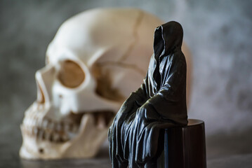 A statue of a grim reaper sitting and skull  background.
