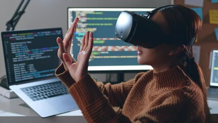 Young Asian woman, developer programmer, software engineer, IT support, wearing virtual reality headset developing and programming VR game application at night overtime.