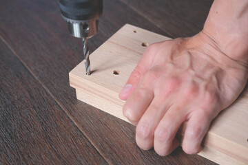 Man drills a holes on wooden board for production handcraft furniture at home. Assembly furniture