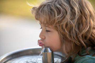 Child drinking water from a water fountain in park.