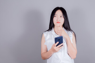 Beautiful asian woman using a smartphone on gray background, holding hand near the face