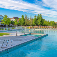 Square Whispy white clouds Large public pool surrounded by lounge chairs and wire fence at...