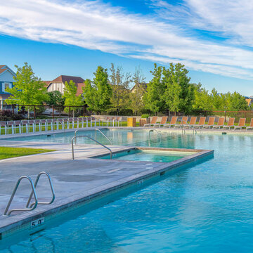 Square Whispy white clouds Large public pool surrounded by lounge chairs and wire fence at Daybreak, Utah