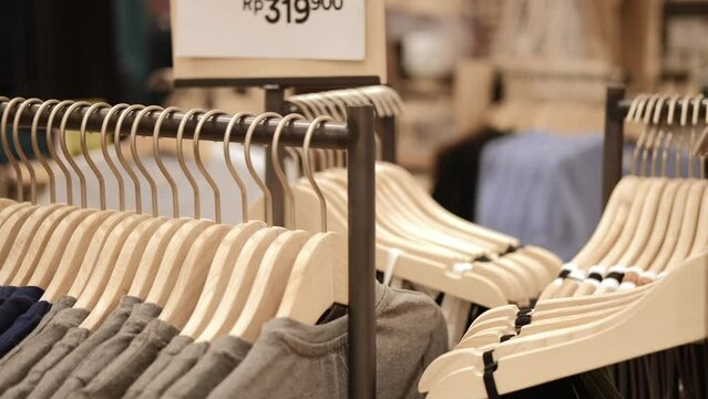 Close-up of hangers with clothes in a store, clothes for sale hang on wooden hangers, a new collection of clothes in different sizes. Industry in the field of clothing trade of famous brands.