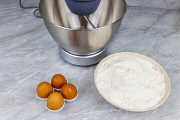 Modern kitchen machine and ingredients for preparing dough (eggs and flour) on a kitchen table