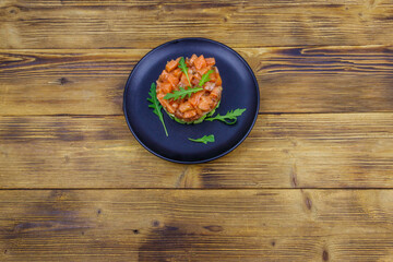 Salmon tartare with avocado and arugula on wooden table. Top view