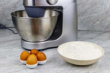 Modern kitchen machine and ingredients for preparing dough (eggs and flour) on a kitchen table