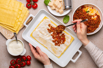 Woman hands Cooking lasagna.  Raw Italian Pasta and ingredients, lasagne flat sheets, meat sauce or ragù bolognese, ground meats and tomato sauce, parmesan cheese,  Béchamel sauce. Top view. - obrazy, fototapety, plakaty