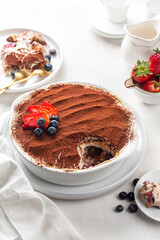 Eating Tiramisu with strawberries and blueberries and berry layer, Italian dessert with ladyfinger biscuits, coffee and marscapone cheese in a casserole, powdered with cacao. Homemade.