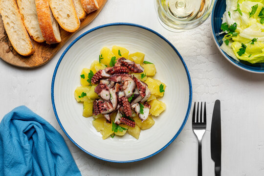 Seafood Dinner. Traditional Italian Octopus and Potato Salad. Insalata di polipo e patate. Bread, white wine, and salad. White table.