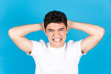 Angry and despaired hispanic teenager boy hands on head isolated on blue background.