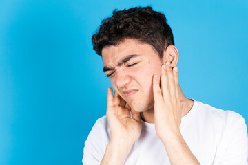 Hispanic teenager boy suffering earache isolated on blue background.