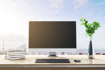 Close up of modern designer desktop with books, empty computer screen, decorative plant, supplies and bright city and sky view background. Mock up, 3D Rendering.