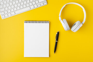 Workspace surface. Notebook, pen, headphones and portable keyboard on yellow background, flat lay