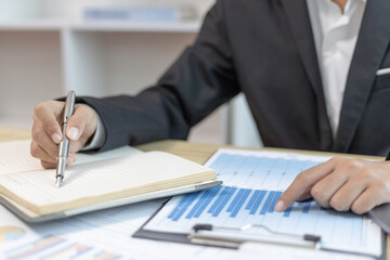 Head of marketing is recording the company's financial growth statistics using graphs as a reference for reviewing and analyzing the results, Taking notes and analyzing data graphs in office.