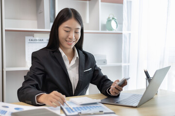 Finance workers are reviewing the company's financial data on a laptop and using smartphones to communicate or chat with the team during social distances, Talk to coworkers over the phone.