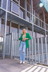 A blonde model woman in a green jacket in a beautiful building in the city. Summer vacation lifestyle