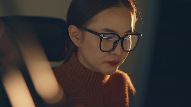 Young Asian woman, developer programmer, software engineer, IT support, wearing glasses working hard at night overtime on computer to check coding in bugging system.