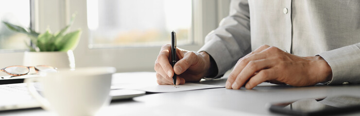 Young man signing an official document, male hand holding pen putting signature at paper contract agreement. Business, lawyer, finance, notary, trading, loan, accounting concept. Banner