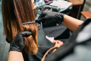 Close up of hairstylist combing woman's long hair during appointment at hair salon.