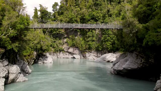 Stunning view, natural wonder of pristine water in canyon native forest at Hokitika Gorge. Drone flying under swing bridge.