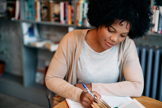 Black Mid Adult Woman Writing Notes While Doing Research At University Library.