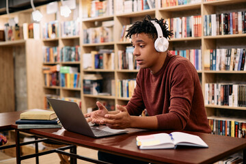 Black male student making video call via laptop while learning in library,