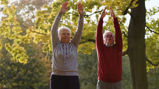 Lovely caucasian heterosexual couple of pensioner seniors exercising, stretching in park, taking care of their physical wellbeing. High quality photo