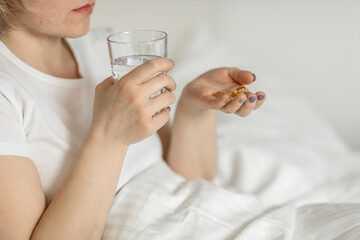 A white faceless woman, a middle-aged woman holds a glass of clean water and vitamins in her hands, sitting on the bed. the concept of health and beauty care