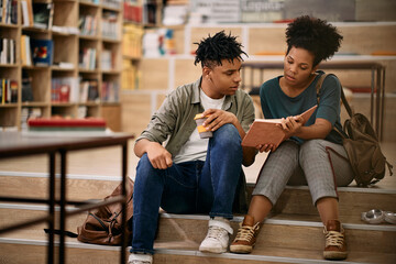 African American adult students reading book together at university library.