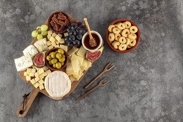 Tasty cheese board with berries, honey, nuts, olives, and cheese varieties on a wooden kitchen plate. Party snack food, copy space.