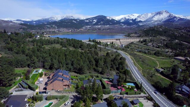 Smooth cinematic push in aerial over the town of Navacerrada towards the reservoir and the snow-capped mountains.