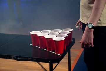 Close-up of people throwing ball into red plastic beer cups. Playing beer pong at the party on dark background 