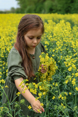 a cute six-year-old girl in a khaki cotton dress stands in a rapeseed field 
