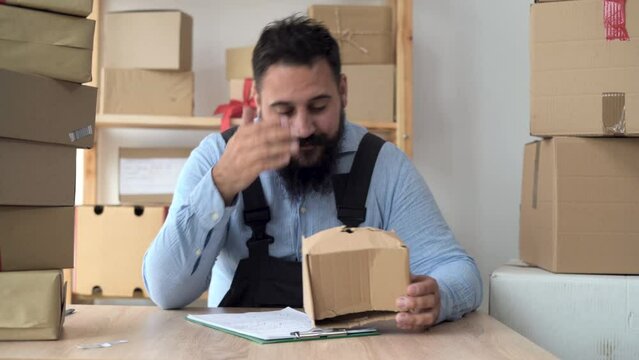 bearded hindu male business owner working from home in uniform with packing box at workplace - online buying or selling online concept. Counts boxes of goods and keeps records.