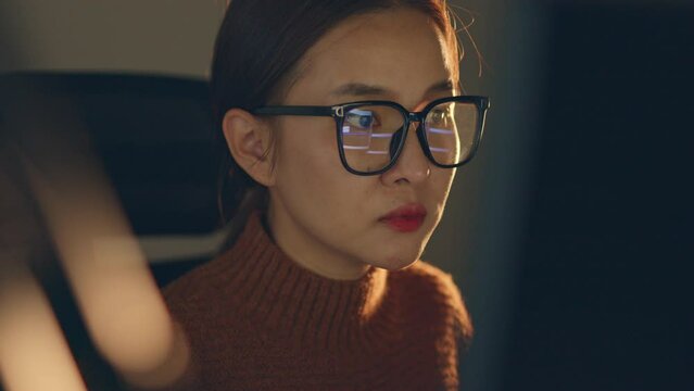 Young Asian woman, developer programmer, software engineer, IT support, wearing glasses working hard at night overtime on computer to check coding in bugging system and running program successful.