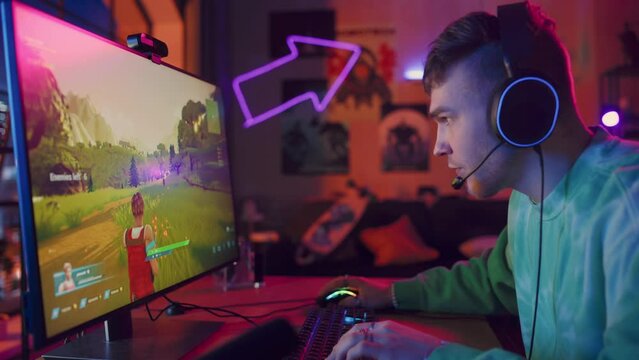 Joyful Gamer Playing PvP Shooter Video Game in Which Players Fight in a Battle Royale Deathmatch on His Personal Computer. Room and PC with Colorful Neon Led Lights. Stylish Man in Cozy Room at Home.