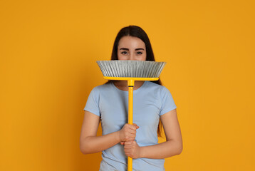 Beautiful young woman with broom on yellow background