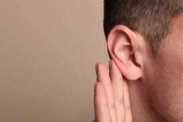 Man showing hand to ear gesture on beige background, closeup. Space for text