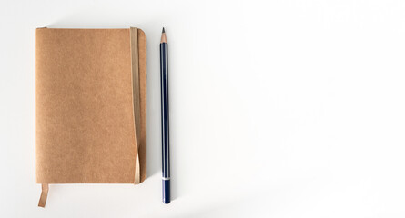 top down view of small brown notebook and sharp pencil on white desk