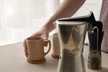 a man prepares coffee on the table a geyser a coffee grinder and two mugs