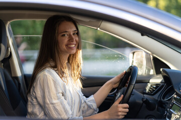 Fototapeta na wymiar Happy young girl sitting on driver seat in new car joyful smiling hold hands on wheel. Cheerful female driving vehicle looking through open window. Successful woman car owner or getting driver license