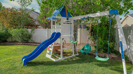 Panorama Whispy white clouds Small set of playground on a green lawn at the fenced backyard a