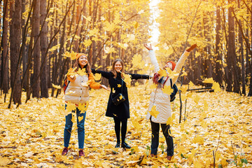 a group of friends are having fun and toss yellow leaves in an autumn park. Fall season activities