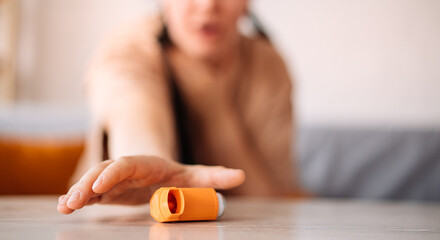 A girl suffering from an asthma attack due to allergies reaches for an inhaler while sitting on the sofa in the living room of the house. the concept of allergy control