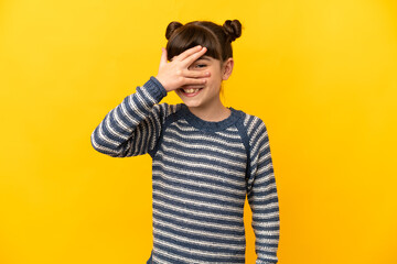 Little caucasian girl isolated on yellow background covering eyes by hands and smiling