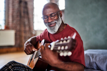 Smiling mature man playing string instrument at home