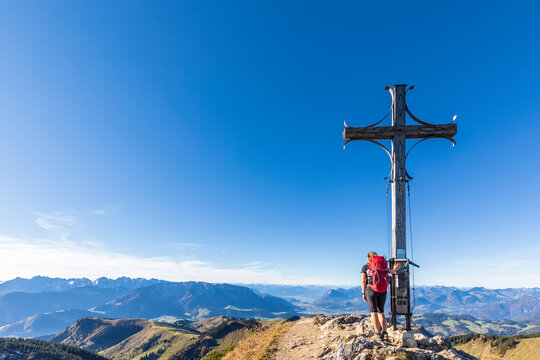 Germany, Bavaria, Female hiker standing by summit cross on Geigelstein mountain
