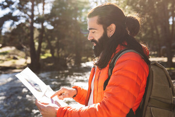 Bearded man wearing backpack reading map in forest